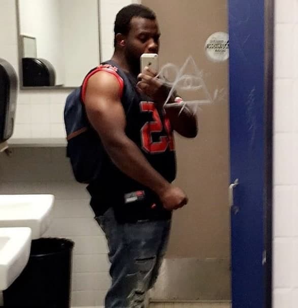 Man taking a mirror selfie with a phone, wearing a navy sleeveless jersey and a backpack.